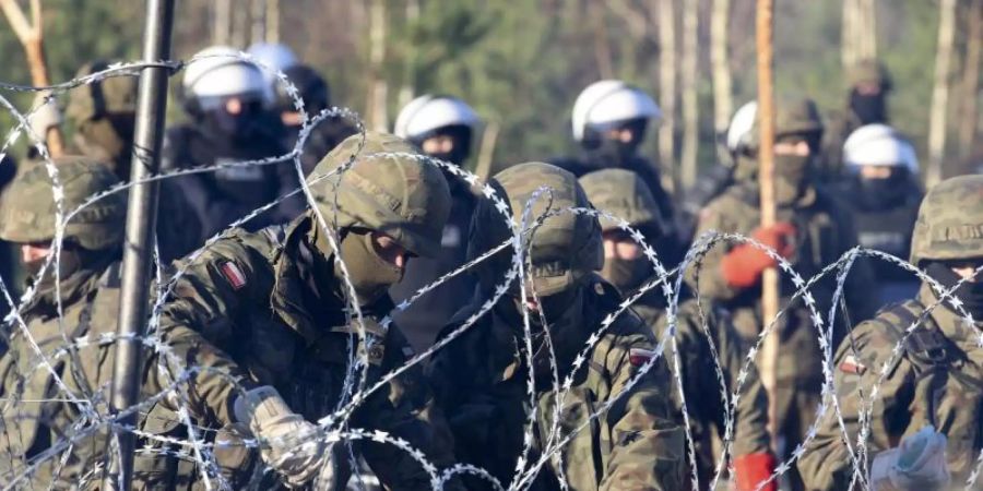 Polnische Polizisten und Grenzschützer stehen in Grodno am Stacheldrahtzaun. Foto: Leonid Shcheglov/BelTA/dpa