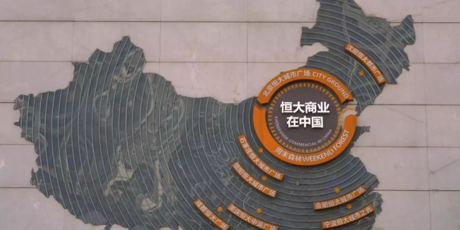 Eine Aufsichtsperson steht neben einer Karte in Peking, auf der die Evergrande-Entwicklungsprojekte abgebildet sind. Foto: Andy Wong/AP/dpa