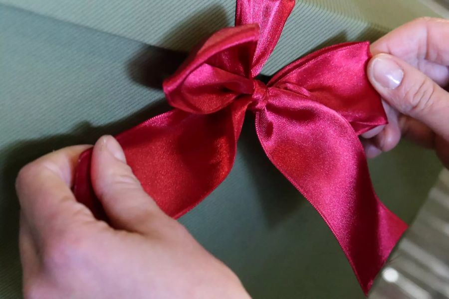 Hand bindet Schleife rotes Geschenkband grünes Papier