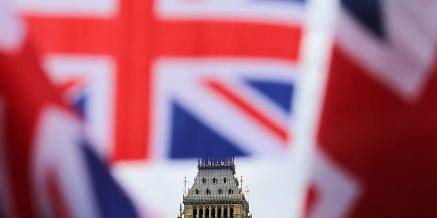 ARCHIV - Britische Fahnen wehen vor dem berühmten Uhrturm Big Ben. Das britische Parlament stimmt am Mittwoch (30.12.2020) über den Brexit-Handelspakt mit der Europäischen Union ab. Beide Kammern sollen die Vereinbarung innerhalb weniger Stunden abnicken. Foto: Michael Kappeler/dpa