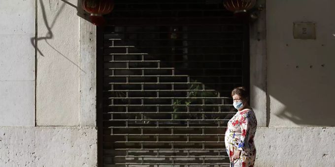 Eine Frau mit einer Gesichtsmaske geht an einem geschlossenen Restaurant in der Innenstadt vorbei. Foto: Armando Franca/AP/dpa portugal