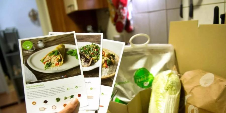 Ein Mann hält mitgelieferte Kochrezepte aus einer HelloFresh Kochbox in der Hand. Foto: picture alliance / dpa