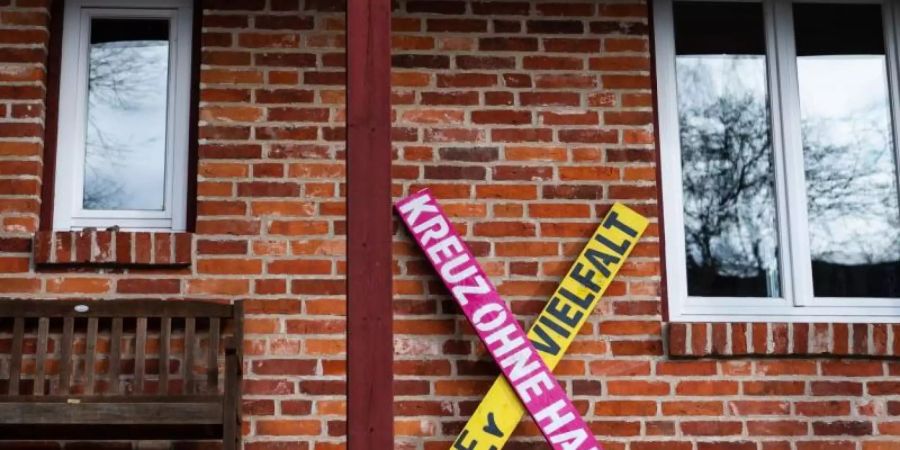 Ein Holzkreuz mit der Aufschrift «Kreuz ohne Haken - fuer Vielfalt» steht an einer Hauswand in Haarstorf im Kreis Uelzen. Dort wehren sich Anwohner seit längerem gegen rechte Siedler. Foto: Philipp Schulze/dpa