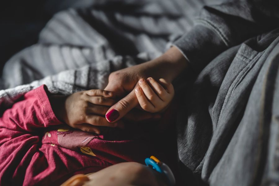 Mutter hält Kinderhand im Bett