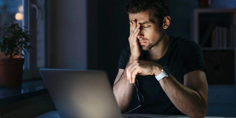 Müder Mann sitzt vor Laptop und hat viel Arbeit