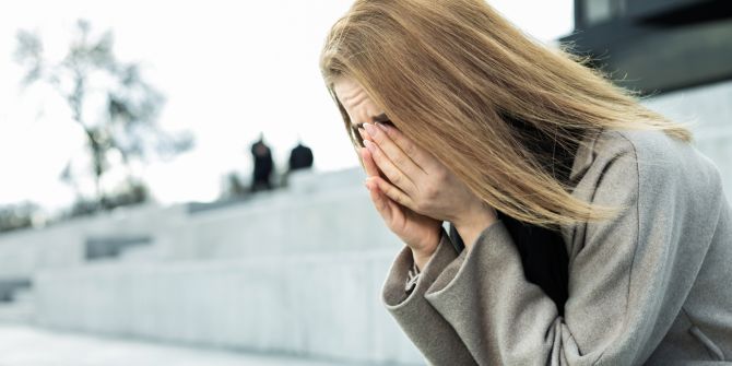 Verzweifelte Frau hält sich Hände vors Gesicht, sitzt auf einer Treppe
