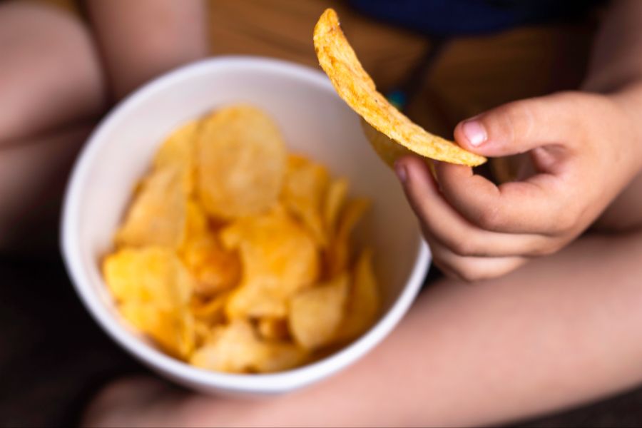 Hand einer Person, die Chips aus einer Schüssel isst