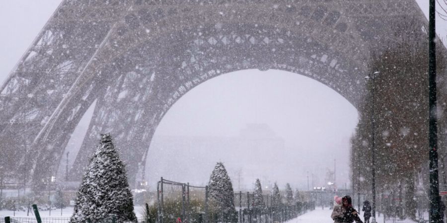 dpatopbilder - Menschen spazieren bei Schneefall in der Nähe des Eiffelturms. Foto: Christophe Ena/AP/dpa