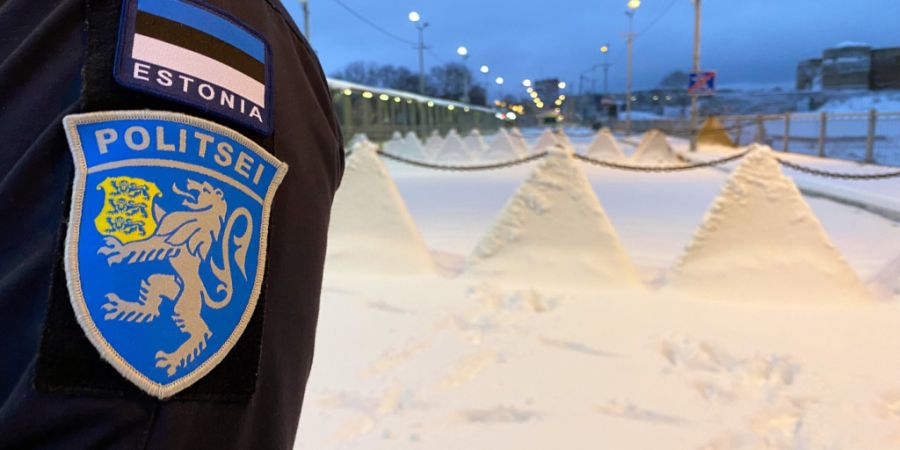 ARCHIV - Ein Wappen der estnischen Polizei und die estnische Flagge sind auf der Uniform eines estnischen Polizisten angebracht, der auf der Grenzbrücke von der estnischen Stadt Narva ...