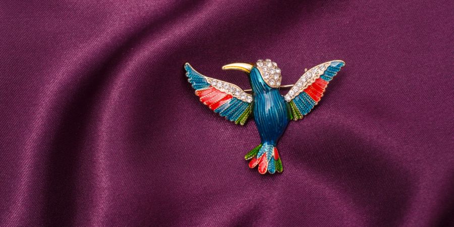 Können einem Outfit das gewisse Extra verleihen: Hier zu sehen ist eine Emaille-Brosche mit Kolibri und Diamanten auf Seidenstoff.