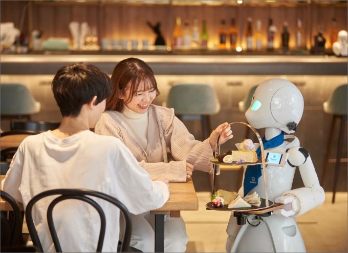 Ein Roboter-Kellner bringt zwei Gästen die Bestellung. roboter