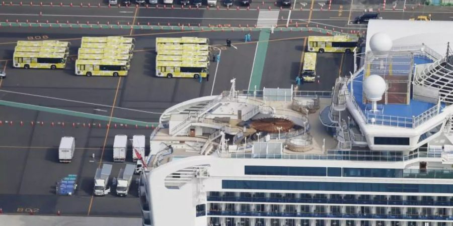 Busse werden in der Nähe des Kreuzfahrtschiffs «Diamond Princess» geparkt. Die ersten Passagiere dürfen von Bord gehen. Foto: Yuta Omori/Kyodo News/dpa