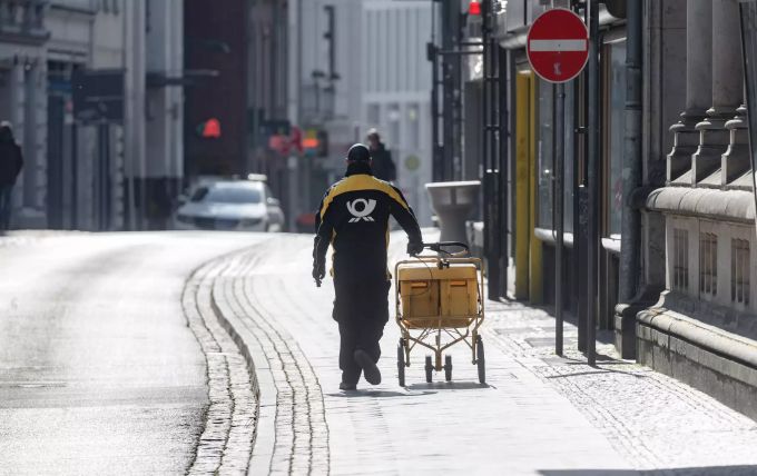 Ein Postbote ist um die Mittagszeit bei schönstem Frühlingswetter in der fast menschenleeren Innenstadt Lübecks unterwegs. Die Kontaktsperren und Ladenschliessungen zur Bekämpfung der Corona-Pandemie halten Einwohner und Touristen fern. Coronavirus - Lübeck