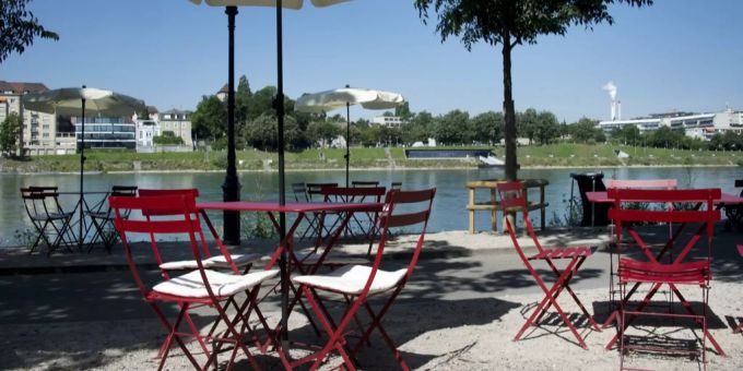 Tische und Stühle stehen vor einer Buvette am Unteren Rheinweg in Basel. oetlinger buvette