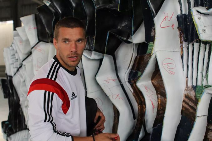 Der deutsche Nationalspieler Lukas Podolski signiert die Skulptur von Pflugi an der Fussball-WM in Brasilien 2014.