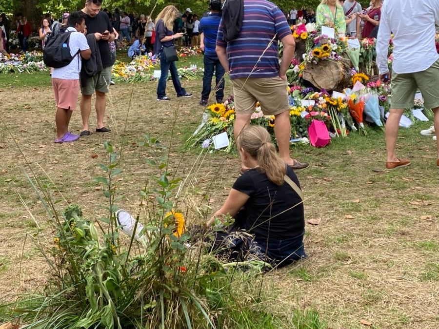 Eine Frau sitzt auf dem Boden vor den Blumen-Tributen.