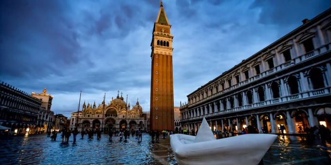 Touristen stehen im Sonnenuntergang auf dem überschwemmten Markusplatz mit Markusturm. Venedig