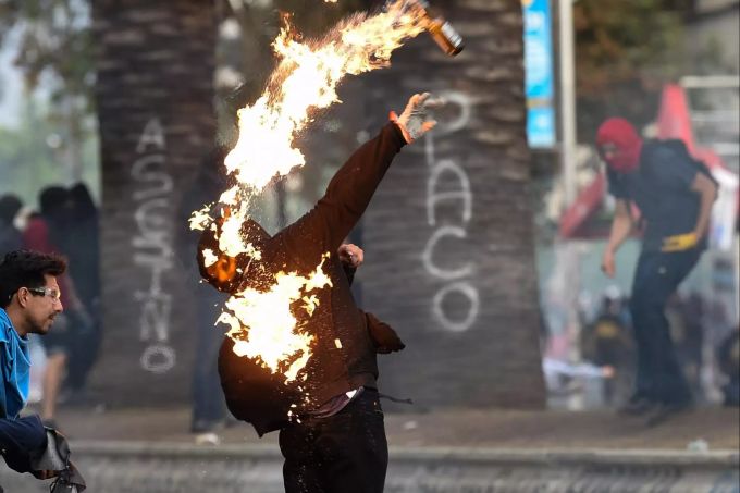 Ein Demonstrant, der einen Molotowcocktail wirft, steht in Flammen. Proteste in Chile