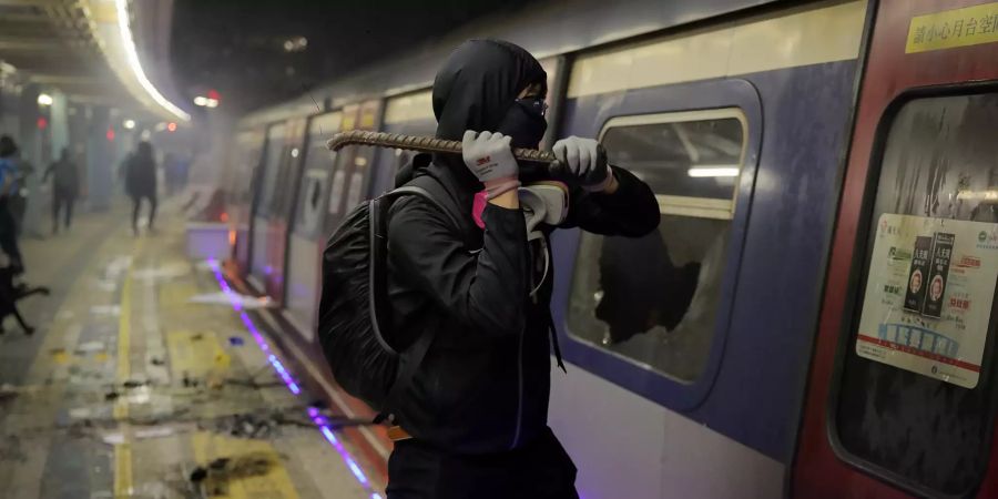 Ein Student schlägt die Scheiben von einem Zug, der im Inneren der MTR-Station der chinesischen Universität geparkt ist, ein. Fünf Monate nach Ausbruch der Proteste gegen die Regierung in Hongkong nimmt die Gewalt kein Ende: Nachdem am Montagmorgen erneut ein 21 Jahre alter Demonstrant von einem Polizisten angeschossen und in den Oberkörper getroffen worden war, spielten sich in der chinesischen Sonderverwaltungsregion teils chaotische Szenen ab. Foto: Kin Cheung/AP/dpa +++ dpa-Bildfunk +++