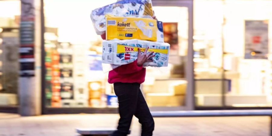 Ein Frau läuft mit dem Arm voller Klopapierrollen aus einem Drogeriemarkt heraus. Foto: Axel Heimken/dpa