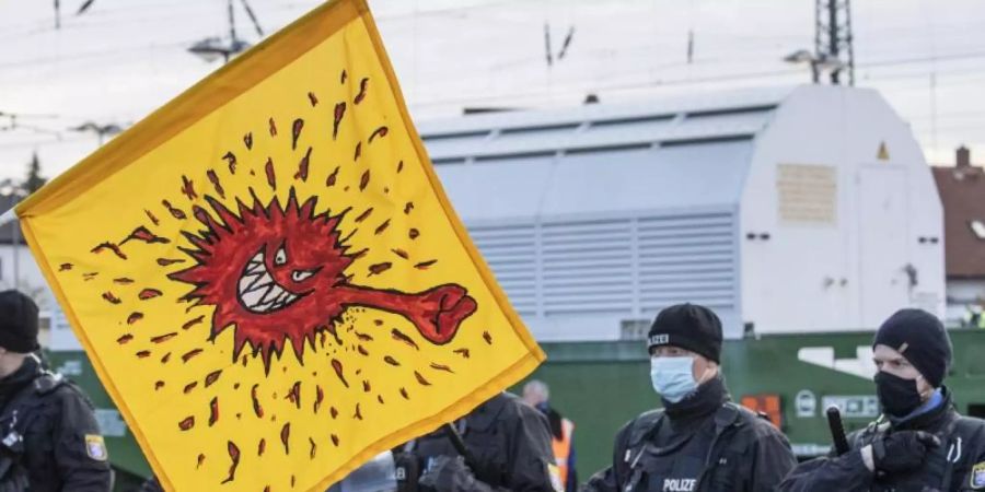 Mit einer Coronavirus-Karikatur auf einer Fahne protestieren Anti-Atomkraft-Gegner in Biblis gegen den Castor-Transport. Foto: Boris Roessler/dpa