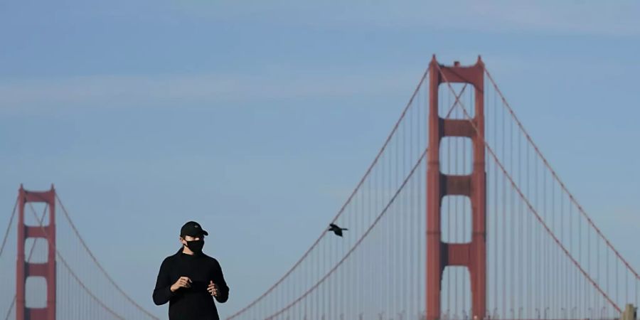 Eine Frau mit Mund-Nasen-Schutz joggt unweit der Golden Gate Bridge in San Francisco. In fünf Bezirken in der Region sind die Bewohner dazu angehalten, ihr Zuhause nicht zu verlassen. Foto: Jeff Chiu/AP/dpa