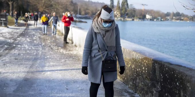 Eine Frau mit Schutzmaske läuft am Ufer des Genfersees. Cold weather in Geneva