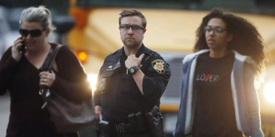Ein Polizist schützt nach der Bluttat Schüler, die vor der angegriffenen Highschool aus einem Bus steigen. Foto: David Zalubowski/AP