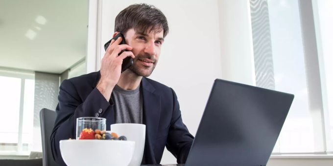 Leistungsfähig durch den Tag: Ein Joghurt mit Obst und Nüssen lässt sich schnell vorbereiten und eignet sich für das Büro und Homeoffice gleichermassen. Mann telefoniert und arbeitet.