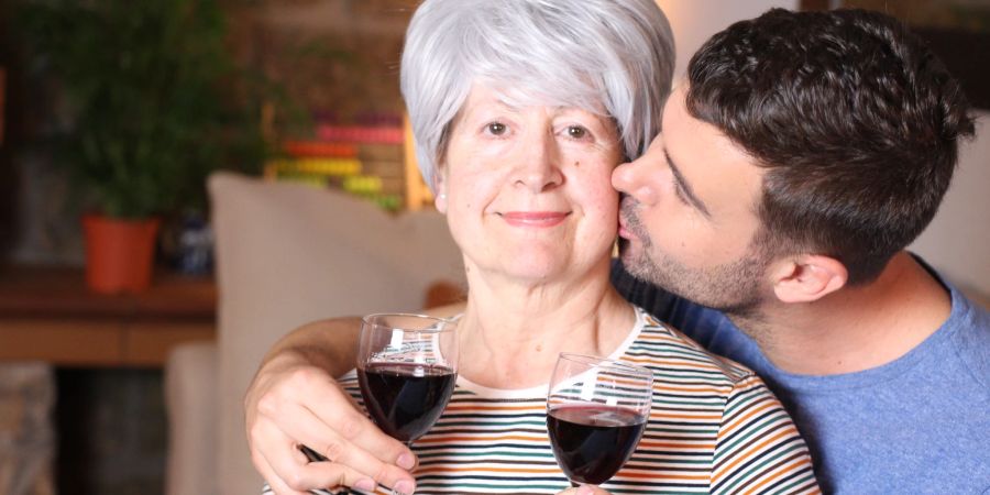 ältere frau mit jüngerem mann, weingläser, im wohnzimmer sitzend