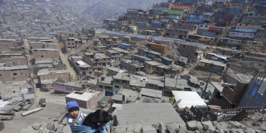 ARCHIV - Eine Frau trägt ihr Kind am Rücken und geht über Steine zu einem Haus in Lima, in dem Essen verteilt wird. Foto: Gian Masko/dpa