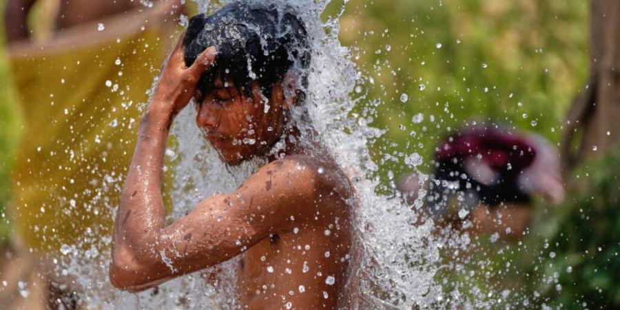 ARCHIV - Ein Junge kühlt sich in der großen Sommerhitze an einem Wasserhahn auf einer Straße in Indien ab. Foto: Channi Anand/AP/dpa/Archivbild