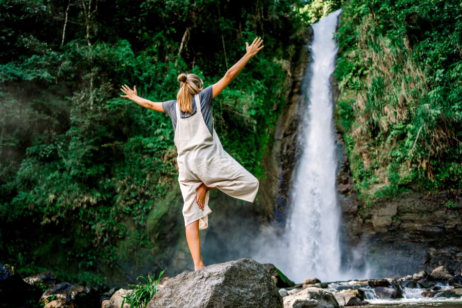 Frau steht vor tropischen Wasserfall und macht Yoga.