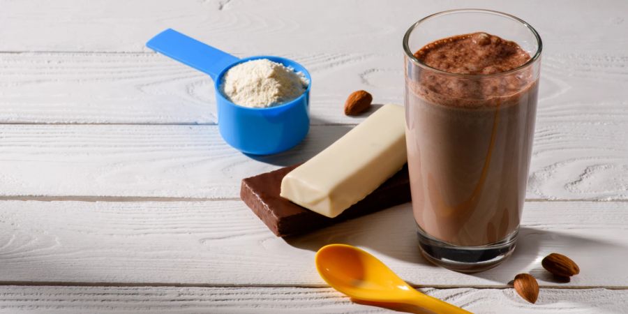 Glas Proteinshake mit Energieriegeln auf weissem Tisch.