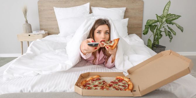 Frau isst Pizza im Bett.