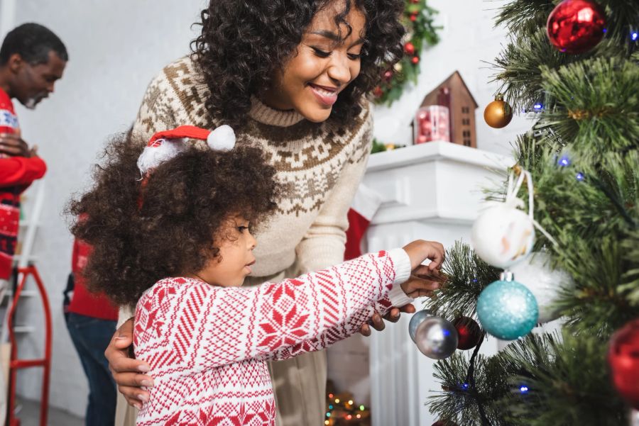 Eine Frau schmückt gemeinsam mit ihrer kleinen Tochter den Weihnachtsbaum.