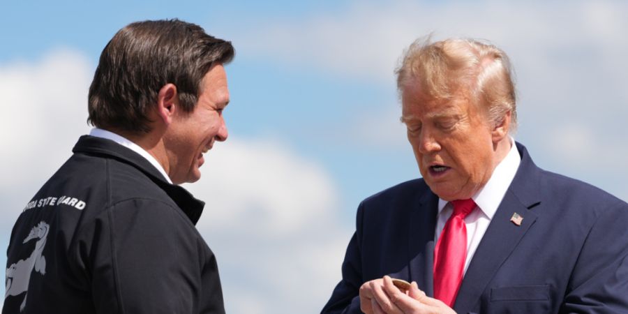 US-Präsident Donald Trump betrachtet eine Münze, die ihm der Gouverneur von Florida, Ron DeSantis (l), überreicht hat, als e mit der Air Force One am Southwest Florida International ...
