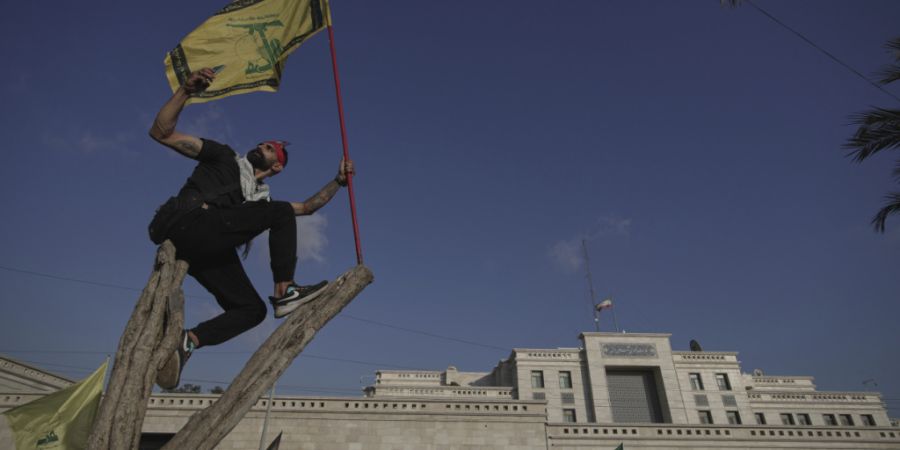 ARCHIV - Ein Hisbollah-Anhänger schwenkt eine Hisbollah-Fahne und macht ein Selfie, während er auf einem Baum vor der iranischen Botschaft in Beirut steht. Foto: Hassan Ammar/AP/dpa