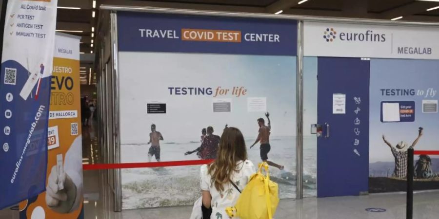 Eine Frau sitzt vor dem Testzentrum am Flughafen von Palma de Mallorca auf Koffern. Foto: Clara Margais/dpa
