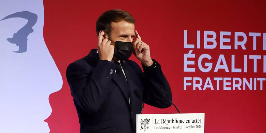 Emmanuel Macron, Präsident von Frankreich, zieht seine Maske an, nachdem er in Les Mureaux eine Rede gehalten hat. Frankreich will nach den islamistischen Terroranschlägen mit vielen Toten in den vergangenen Jahren verstärkt gegen Radikalisierung vorgehen. Foto: Ludovic Marin/POOL AFP/dpa