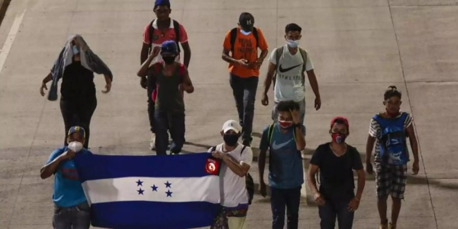 Menschen tragen eine Fahne von Honduras und gehen in der Hoffnung, zukünftig die USA zu erreichen, einen Highway entlang. Foto: Uncredited/AP/dpa