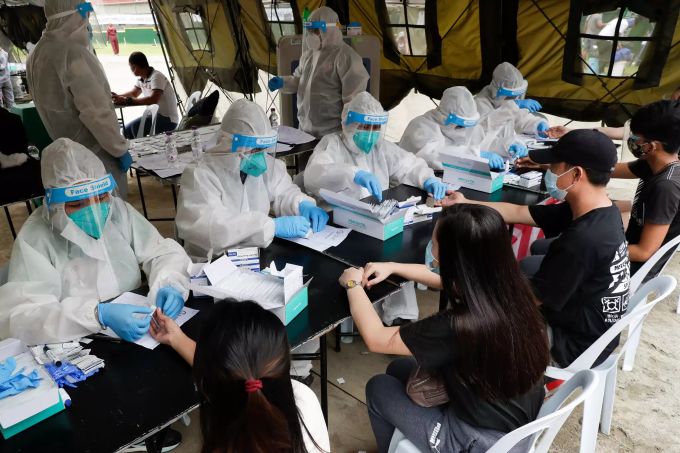 28.07.2020, Philippinen, Manila: Mitarbeiter des Gesundheitswesens tragen Schutzanzüge, während sie in einem Stadion Coronavirus-Schnelltests für Personen durchführen, die die Transporthilfe der Regierung nutzen, um in ihre Provinzen zurückzukehren. Hunderte von Menschen, die aufgrund von Reisebeschränkungen während der Ausgangssperre in der Hauptstadt festsassen, blieben in einem überfüllten Stadion, während sie auf kostenlose Fahrten zurück in ihre Provinzen warteten. Die Gesamtzahl der bestätigten Corona-Fälle auf den Philippinen liegt mittlerweile bei etwa 84 000, mehr als 1900 Menschen sind in Verbindung mit Covid-19 gestorben. Foto: Aaron Favila/AP/dpa +++ dpa-Bildfunk +++ Coronavirus - Philippinen