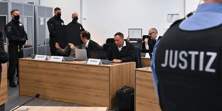 Justizbeamte, Anwälte und die Angeklagten warten im Gerichtssaal auf die Fortsetzung des Prozesses, in dem es um einen Juwelenraub geht.
