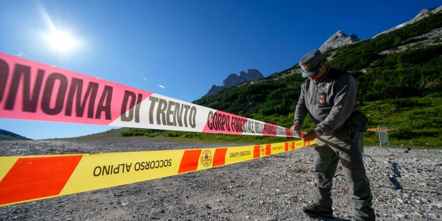 Ein Beamter der italienischen Polizei blockiert den Zugang zum Marmolata-Berg und zum Punta-Rocca-Gletscher in den italienischen Alpen mit Absperrband.