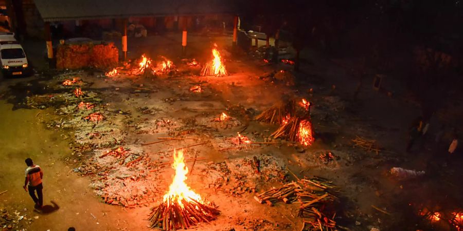 Zwei Männer gehen an Holzfeuern auf dem Gelände eines Krematoriums in Neu Delhi vorbei. Foto: Manish Rajput/SOPA Images via ZUMA Wire/dpa
