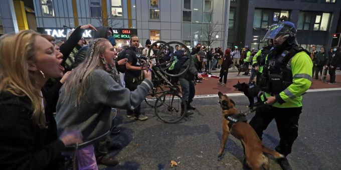21.03.2021, Grossbritannien, Bristol: Ein Polizist mit Polizeihund steht Demonstranten vor der Bridewell Polizeiwache gegenüber. Protest gegen Polizeigesetz in Grossbritannien