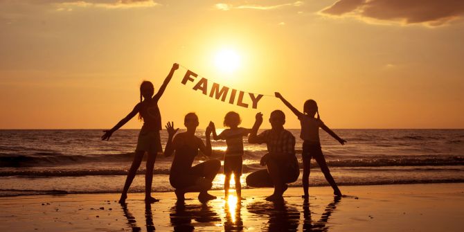 familie am strand hält «family»-schriftzug in den händen, abendsonne