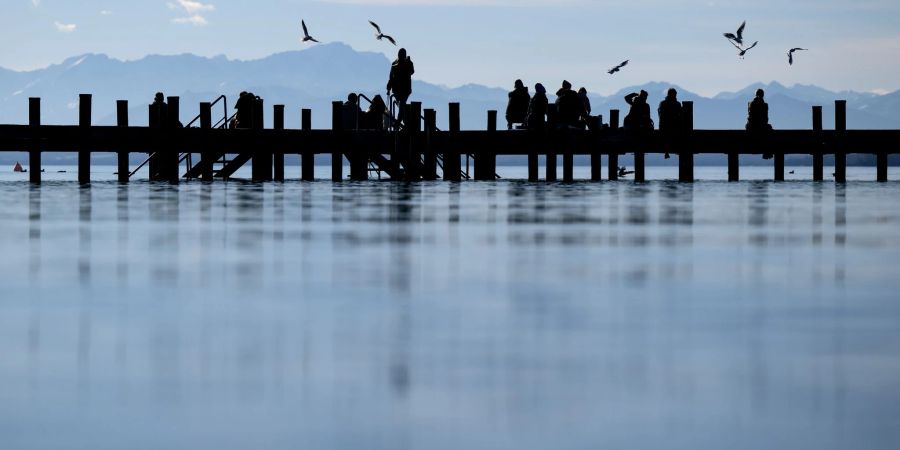 Menschen geniessen das schöne Wetter auf einem Steg am Starnberger See.