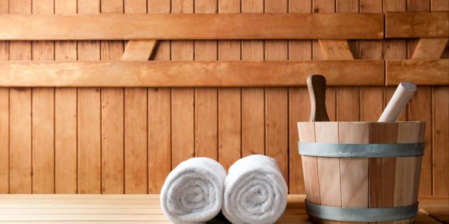 Zwei Handtücher und ein Eimer stehen auf einer Bank in der Sauna.