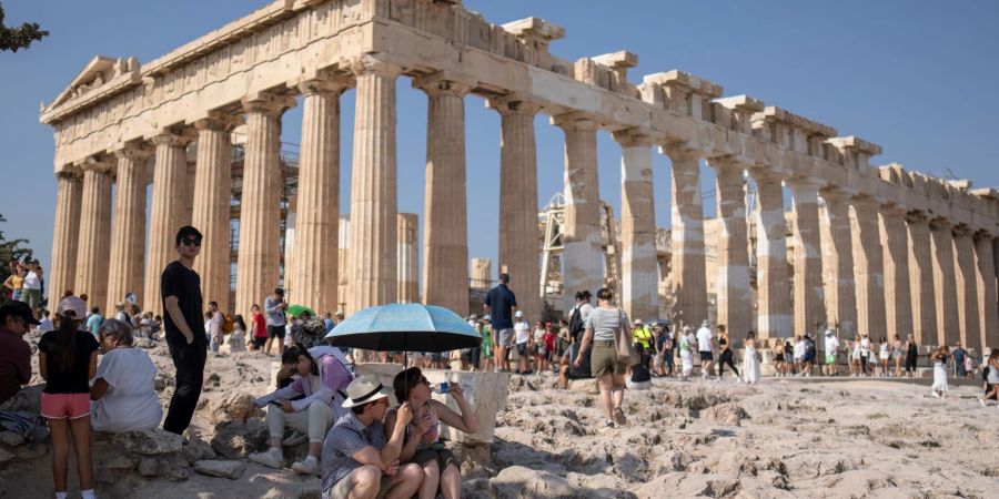 Touristen unter einem Sonnenschirm vor der Akropolis, die inzwischen geschlossen wurde.